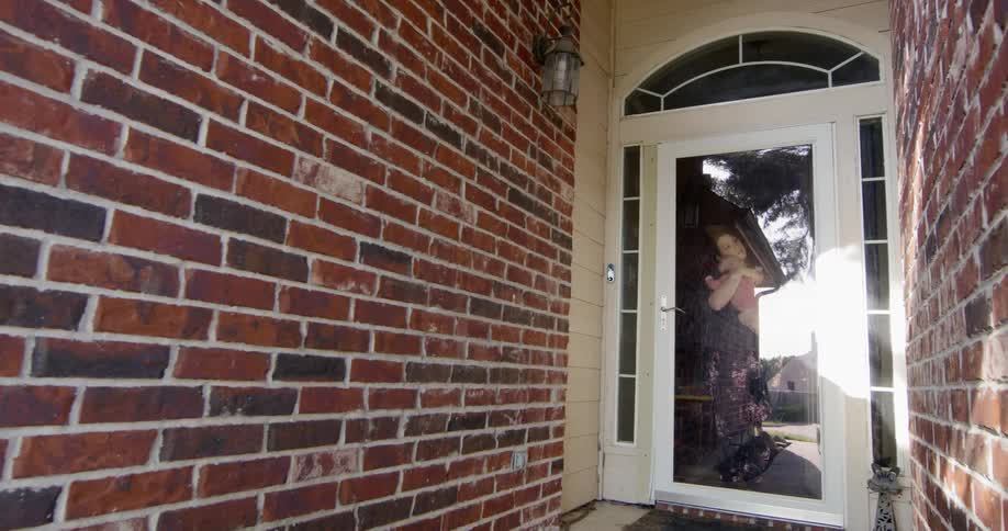 Woman stands near glass door hugging baby