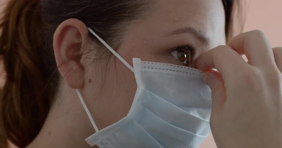 A woman wearing a mask and adjusting it on her face