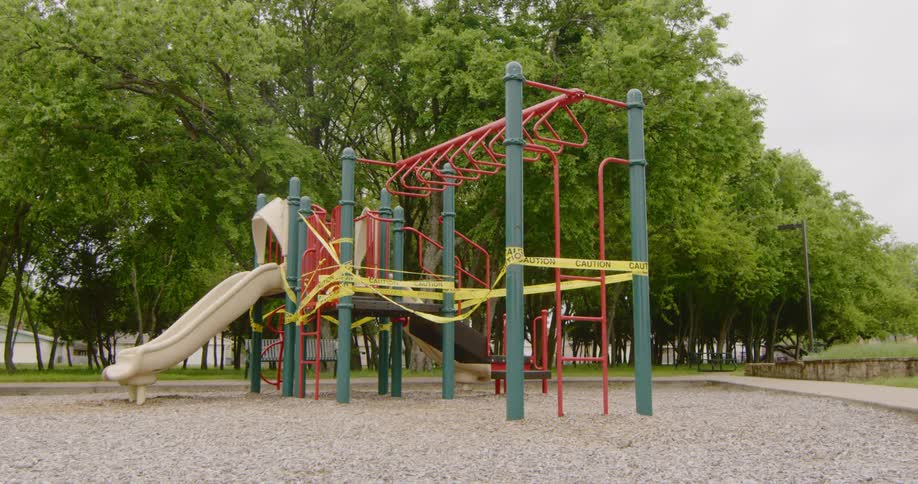 Yellow tape forms barrier around playground equipment in park near trees during the day