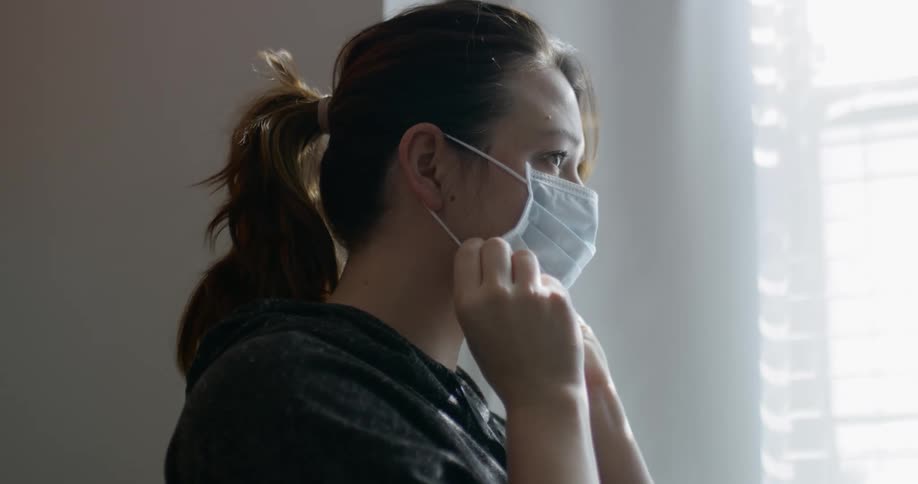 Woman wearing face mask stands near window indoors