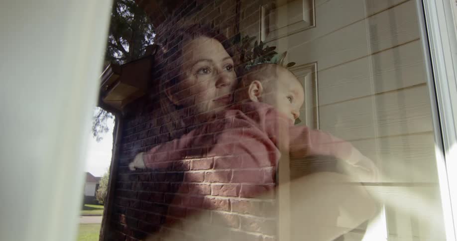 A woman holds a baby standing by a doorway looking outside