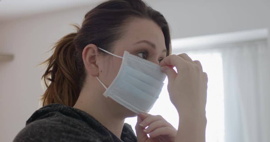 Woman wearing a face mask looks in the mirror at home