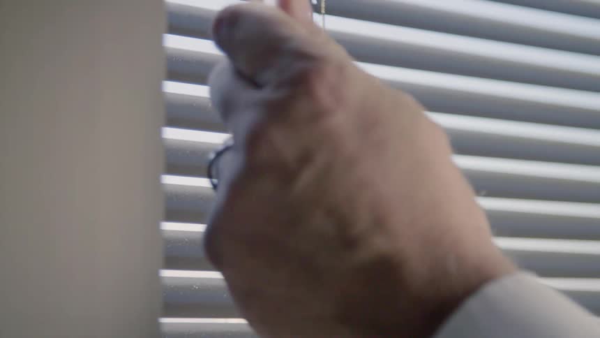 A person spins the mechanism to open up blinds covering a window