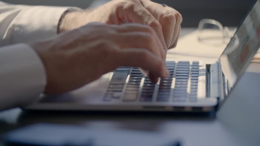 An older white man types on a laptop keyboard