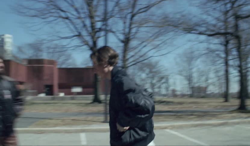A man looks at a monument in a public park and walks away aggressively as his friends watch