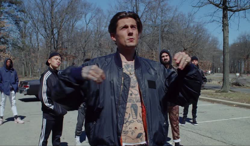 A man walks out of a car and starts talking as a group of men stand around him not moving