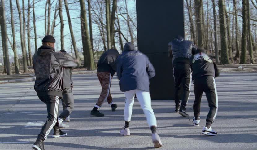 A group of men perform a choreographed dance in a parking lot