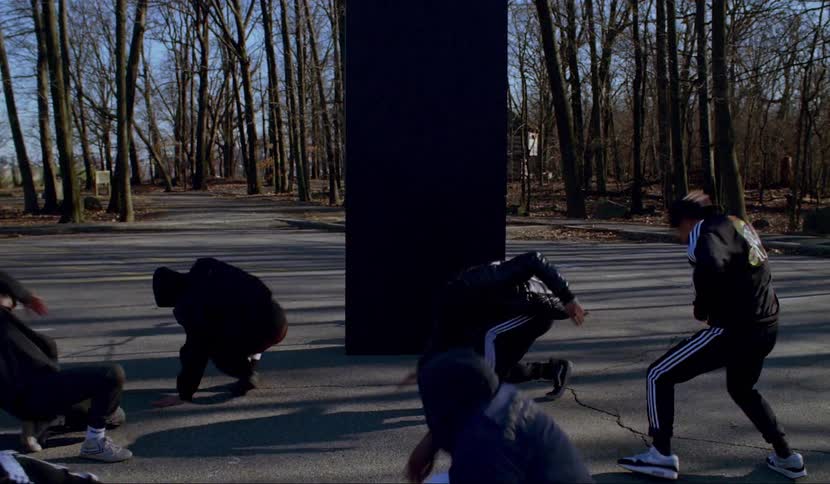 Group of men perform a dance routine on street surrounded by trees