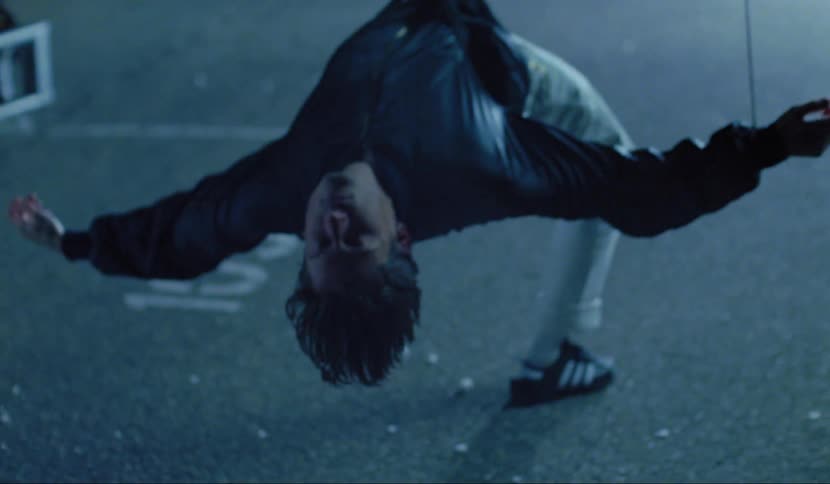 A performer hangs from wire as he bends backward in a parking lot at night