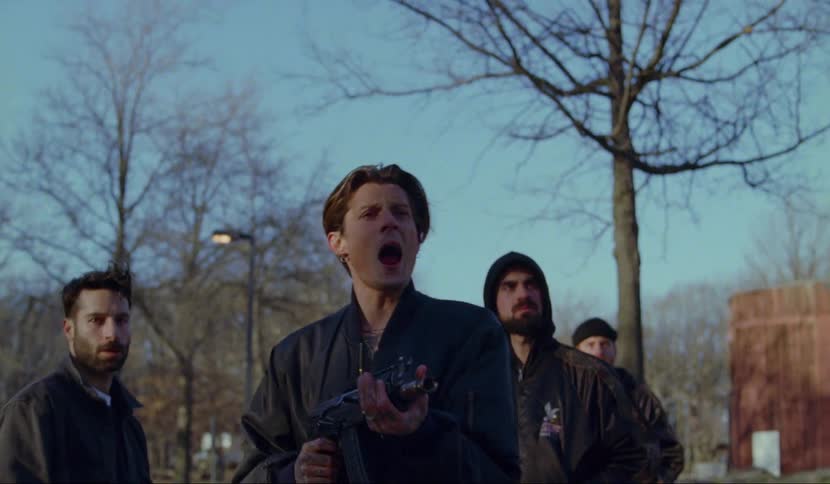 Group of men stand and watch while one of them pretends to fire the machine gun he holds