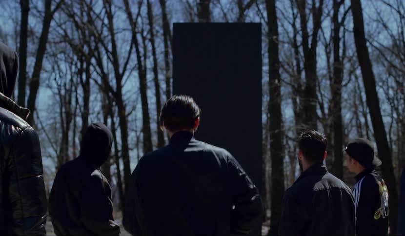 A man walks up to a large black object while others look on