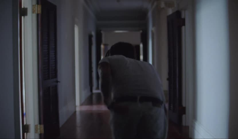 A man with a white shirt and pants stumbling down a hallway