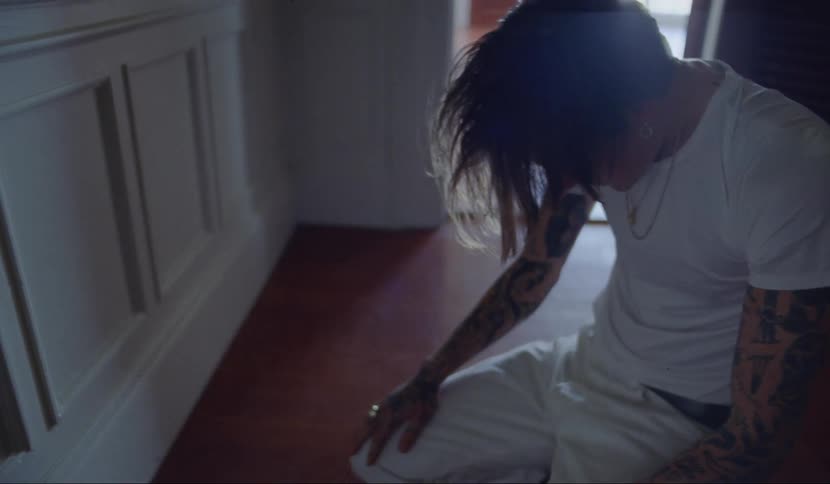 A male teenager sits on the floor while looking down and running his hands through his hair