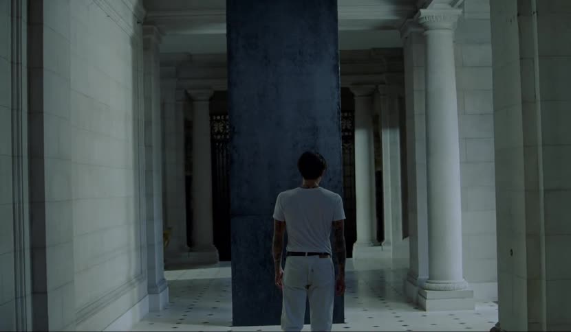 A man walking down a hallway towards a black pillar