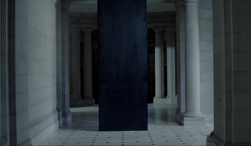 A man panicking and stumbling away from a large black monolith in a hallway
