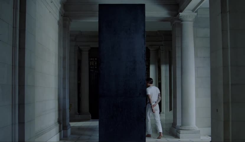 A man walks around a large black panel examining it and staring