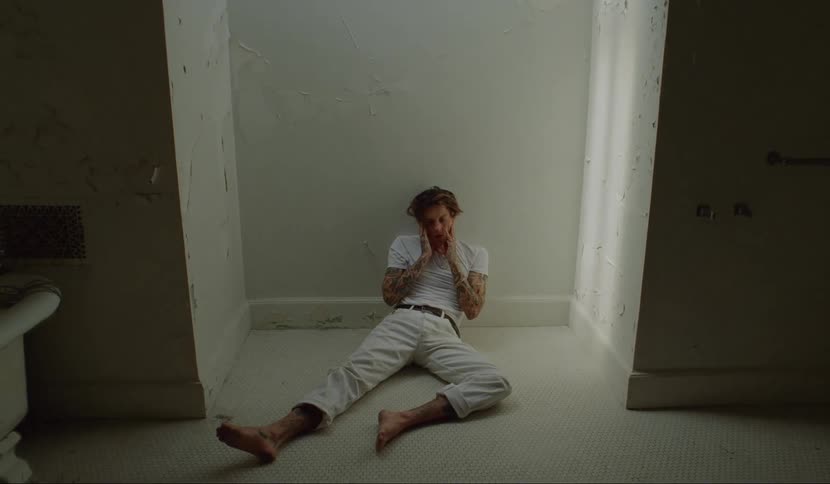 A man sits on a tile floor in a bathroom leaning against the wall looking dejected and needs help