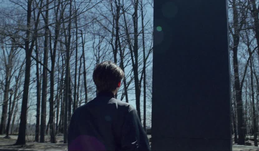 Group of young men stand on parking lot observing a black monolith