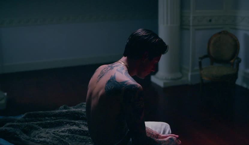A teenager sits on a bed and looks down at his hands