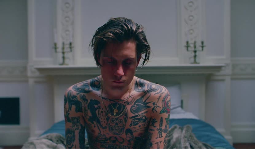 Tattooed man sitting on bed in luxurious room in mansion