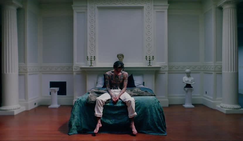A male teenager sits on a bed with his head bowed down