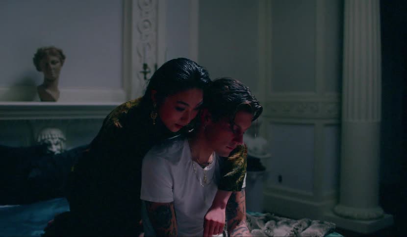 A man sitting on a bed with a woman leaning over and hugging him while she is talking