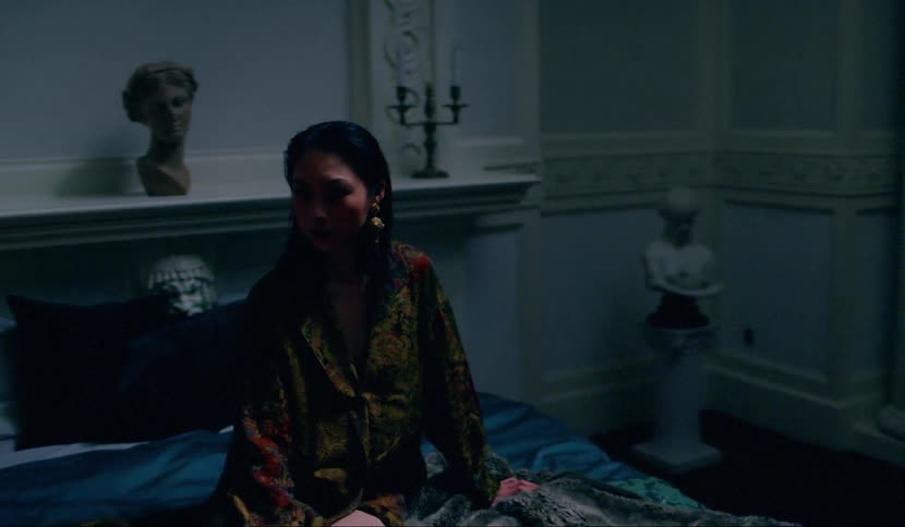 An asian woman in a sleeping robe sitting on a bed in a classically decorated bedroom