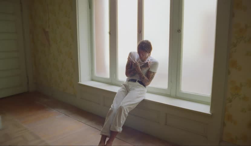 A man sits on a window sill twitching and leaning as if going through withdrawals