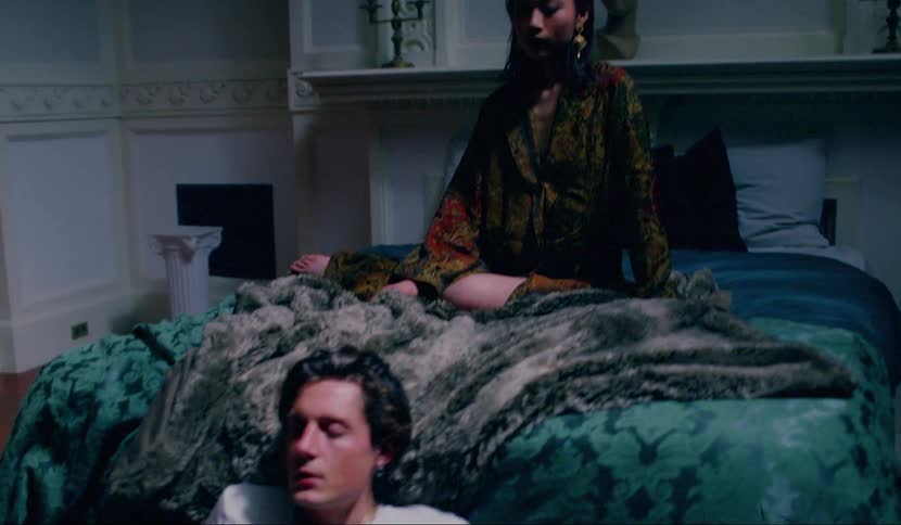 A woman sits on a bed as a male sits on the floor and slams his hands to the ground