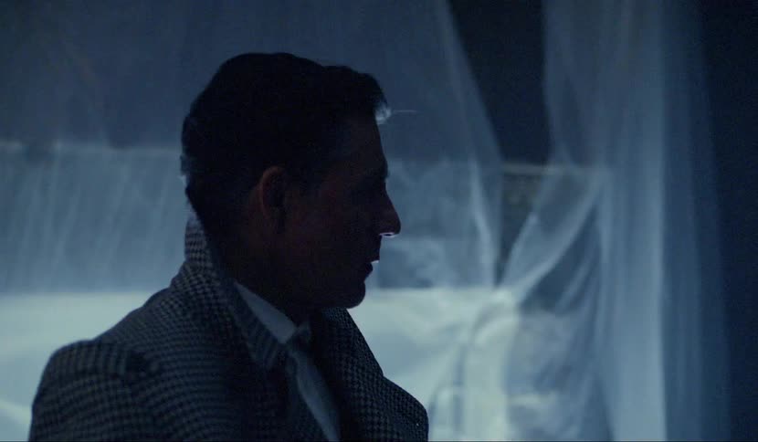 Man in suit stands and looks at a specific point in the dark room