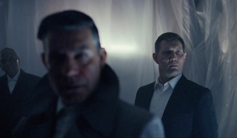 Three men stand apart in a room all dressed in suits