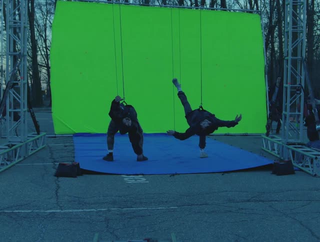 Two men hanging by wires in front of a green screen