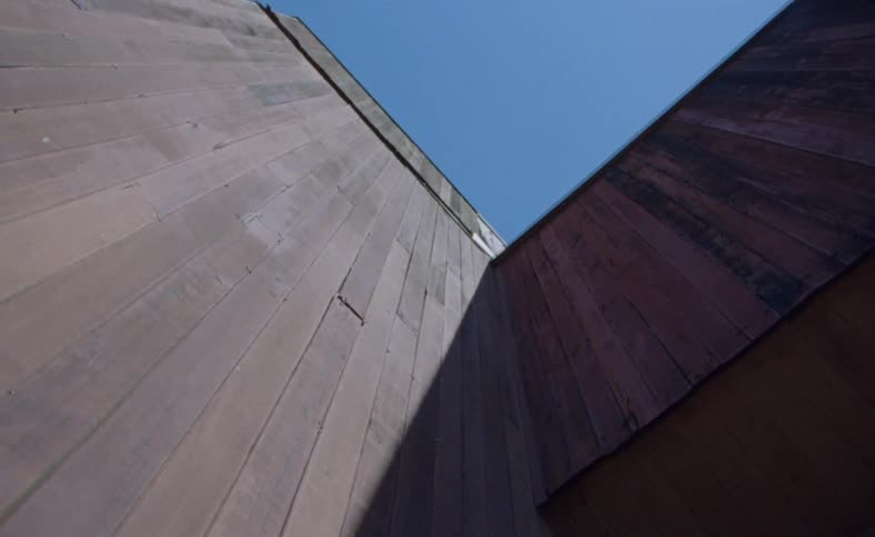 Two wooden walls join to make a corner with the sky above