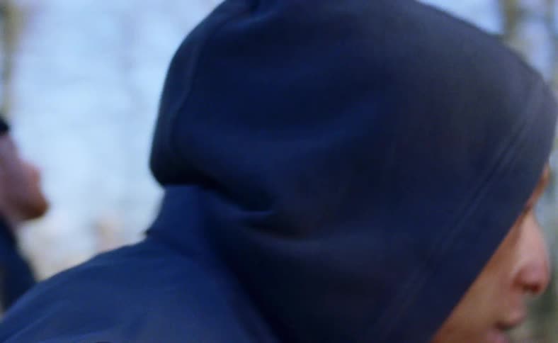 A man wearing a hoodie dances with a group of friends outside on a blue sky day