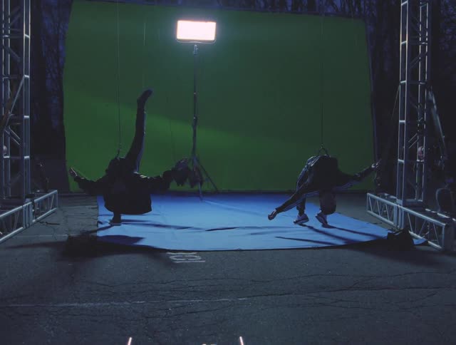 Two people hang near a green screen