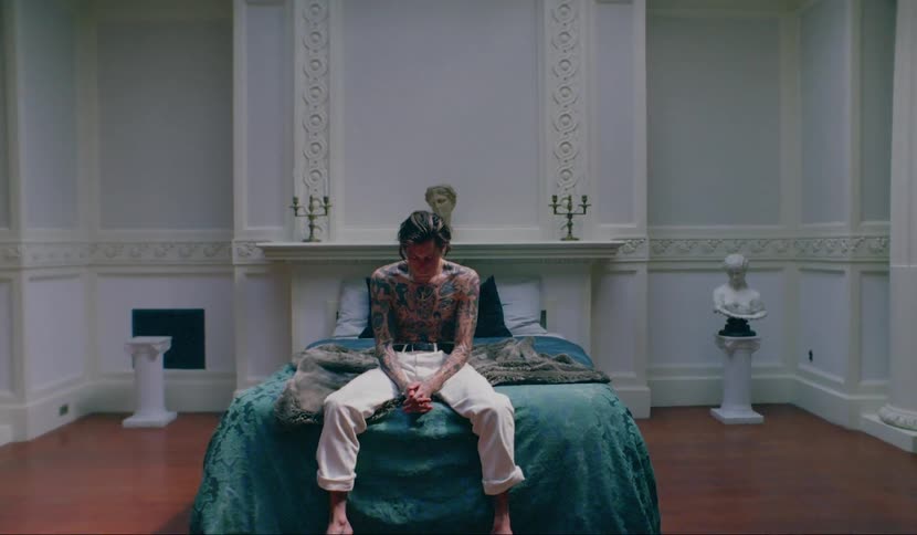 Shirtless tattooed man sitting in bed in a luxurious room