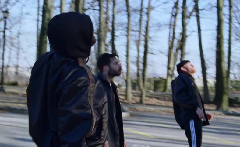 Men twitch and dance outdoors on street among leafless trees