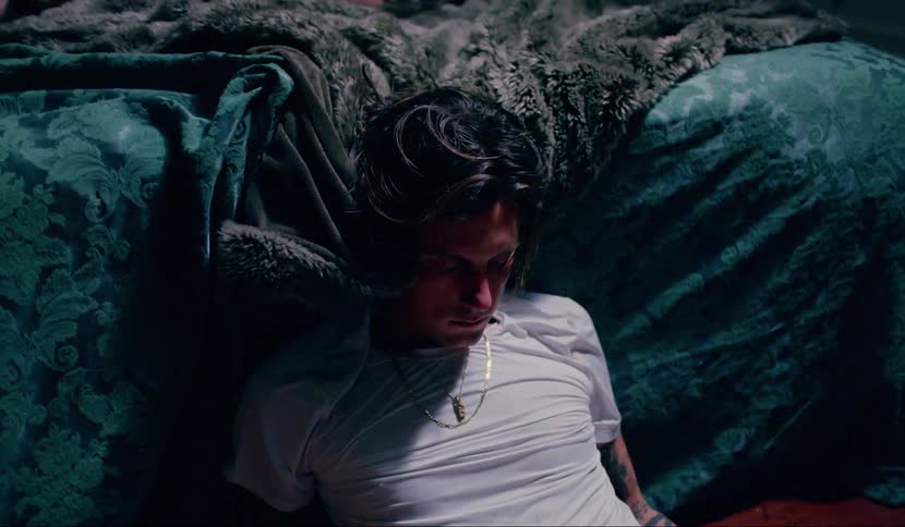 A man sitting on the floor with his back and shoulders leaning against a bed in a dejected manner