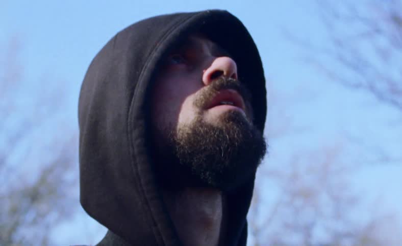 Man wearing a hoodie stands outside looking up