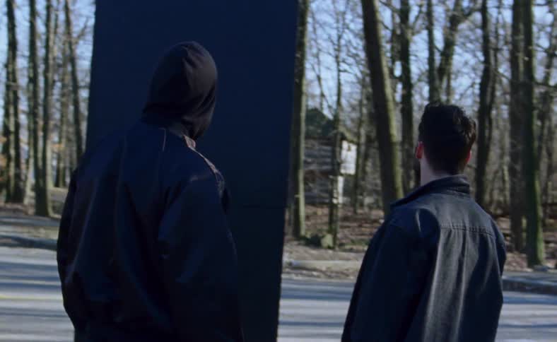 A group of teens stand and look past a big board at an old house
