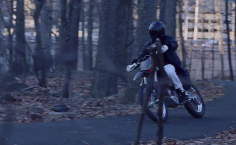 Person rides motorcycle along asphalt path through leafless trees