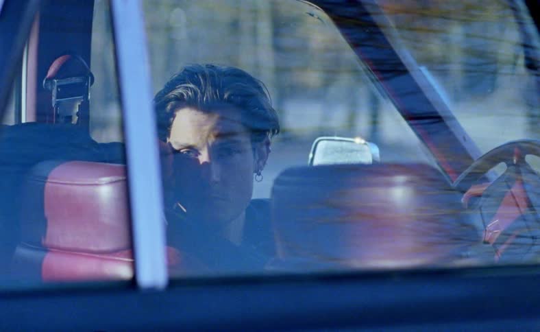 A teenager sits in a car looking around as a man runs by