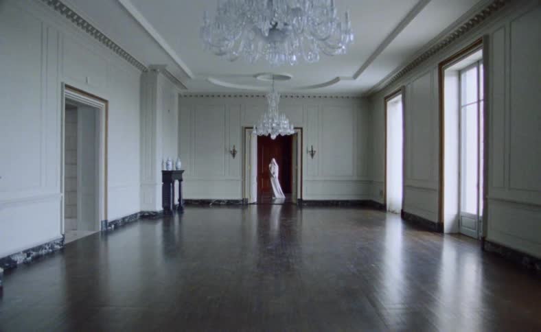 A white statue in an alcove at the end of a ballroom with crystal chandeliers