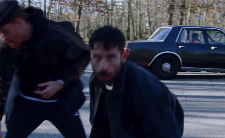 Three men dance on the road next to a black car