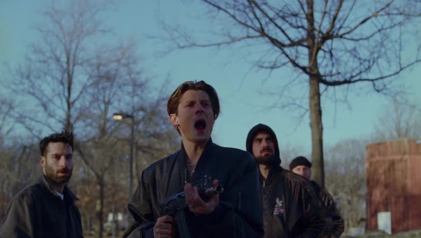 A group of people are standing outdoors and a man is shooting a weapon