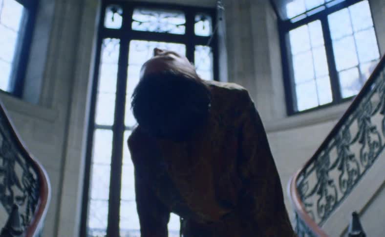 An unconscious asian person hanging at the bottom of a staircase from a metal cable wrapped around their torso