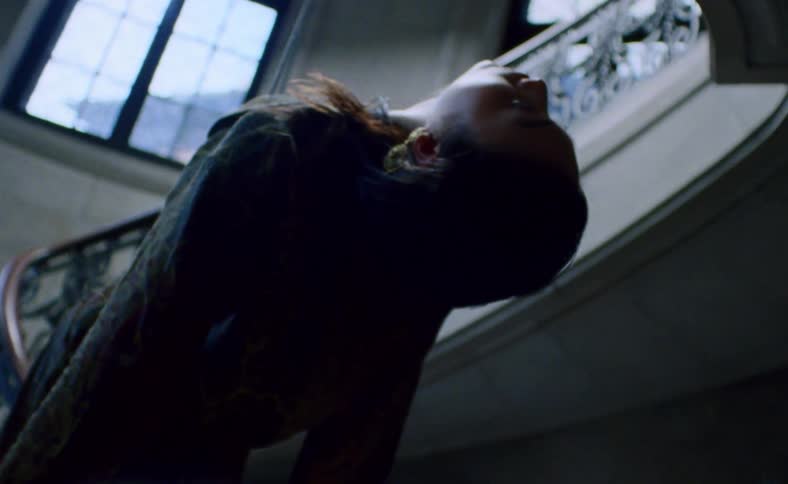 A woman hangs above a staircase from a wire with her back bowed and head back