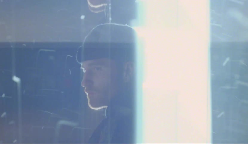 A man stands in front of a door as snow blows around him