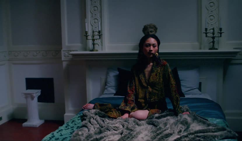 Woman sits on bed in richly patterned robe in ornate bedroom