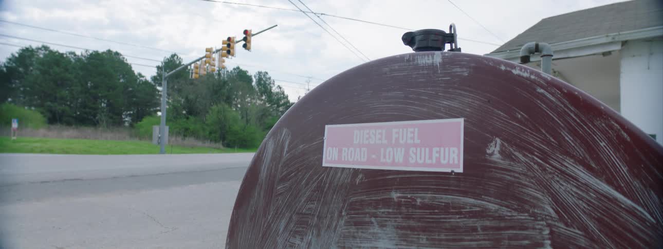 A large outdoor fuel cylinder is next to a gas station by the side of a road